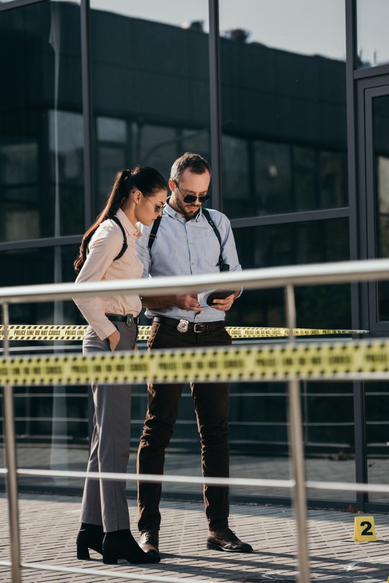 male and female detectives standing at crime scene and looking at notebook